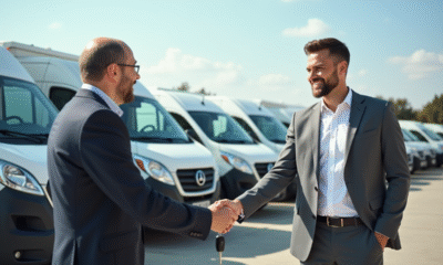 Vendeur souriant remettant les clés à un propriétaire de petite entreprise devant des utilitaires d'occasion